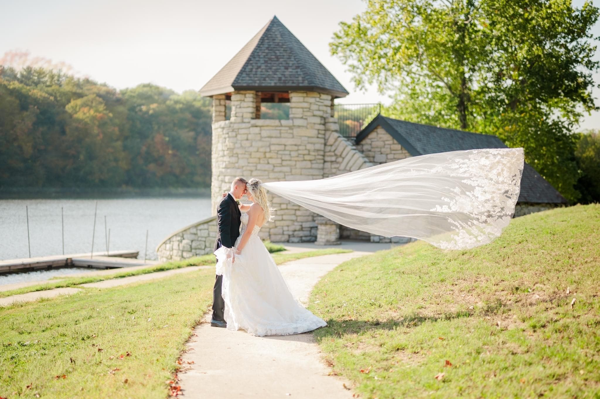 Picture of Bride and groom standing outside of a lighthouse overlooking the water with the brides veil blowing in the wind