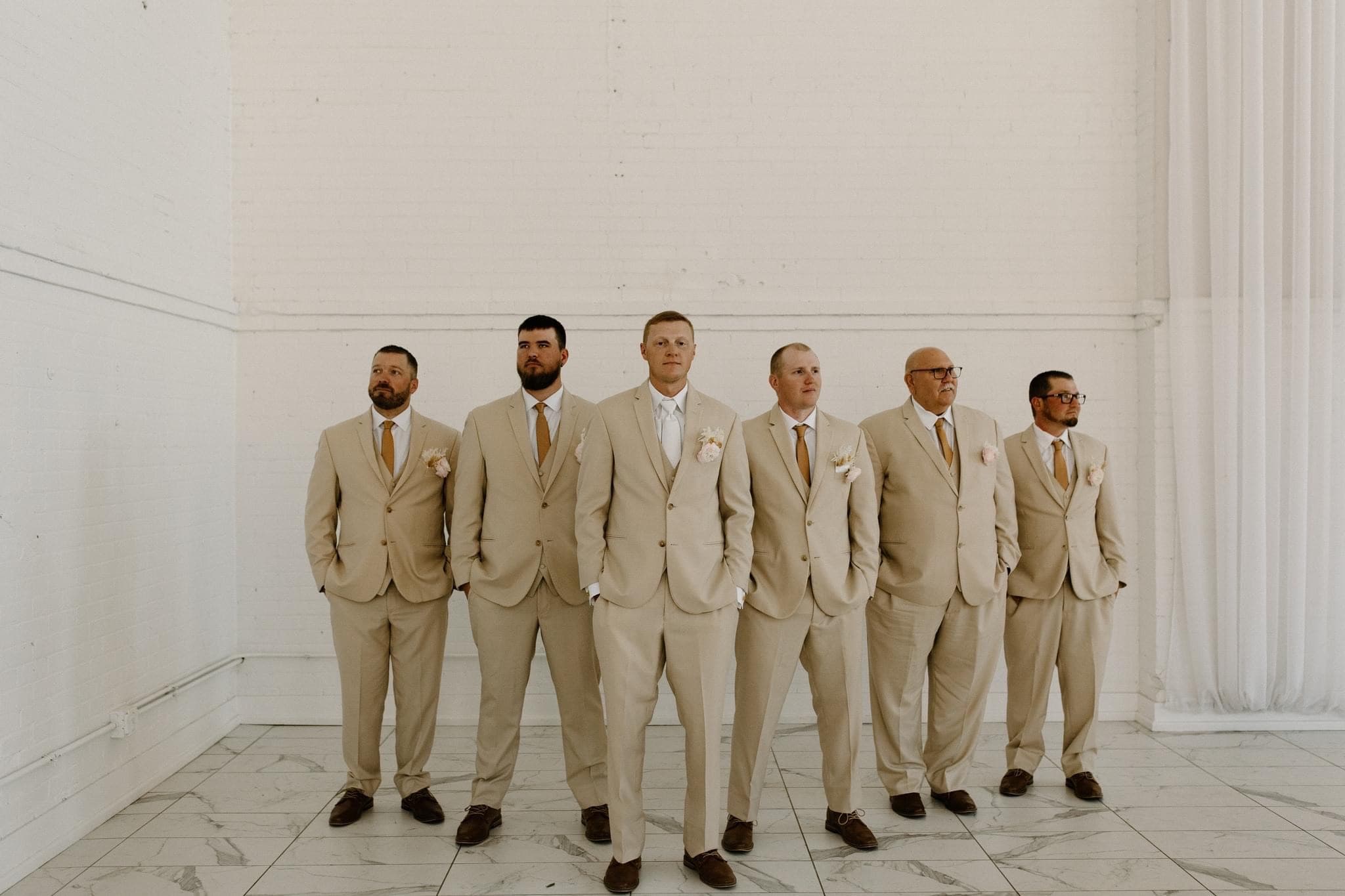 Picture of Groom standing in a triangle formation in front of his groomsmen all wearing matching suits